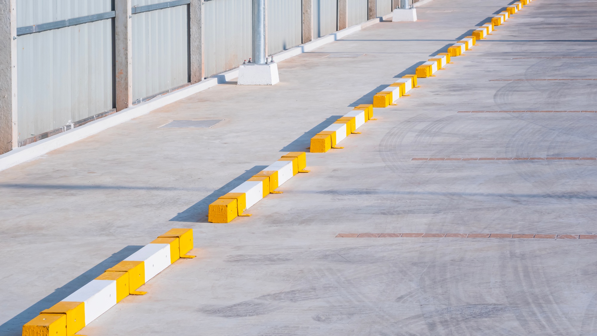 Row of concrete wheel stoppers with yellow and white sign pattern on surface in outdoor parking lot Row of concrete wheel stoppers with yellow and white sign pattern on surface in outdoor parking lot